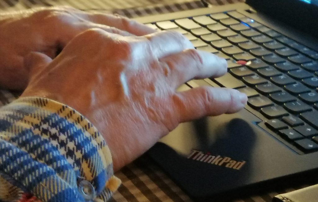 Vanhemman ihmisen kädet tietokoneen näppäimistöllä.
