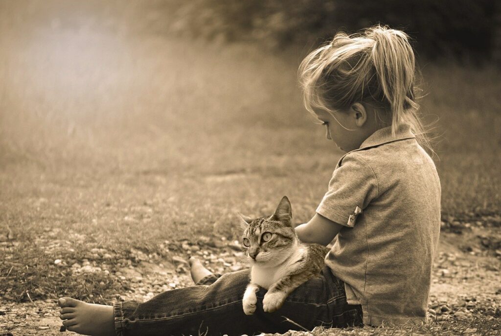Lapsi istuu nurmikolla kissa sylissään.
