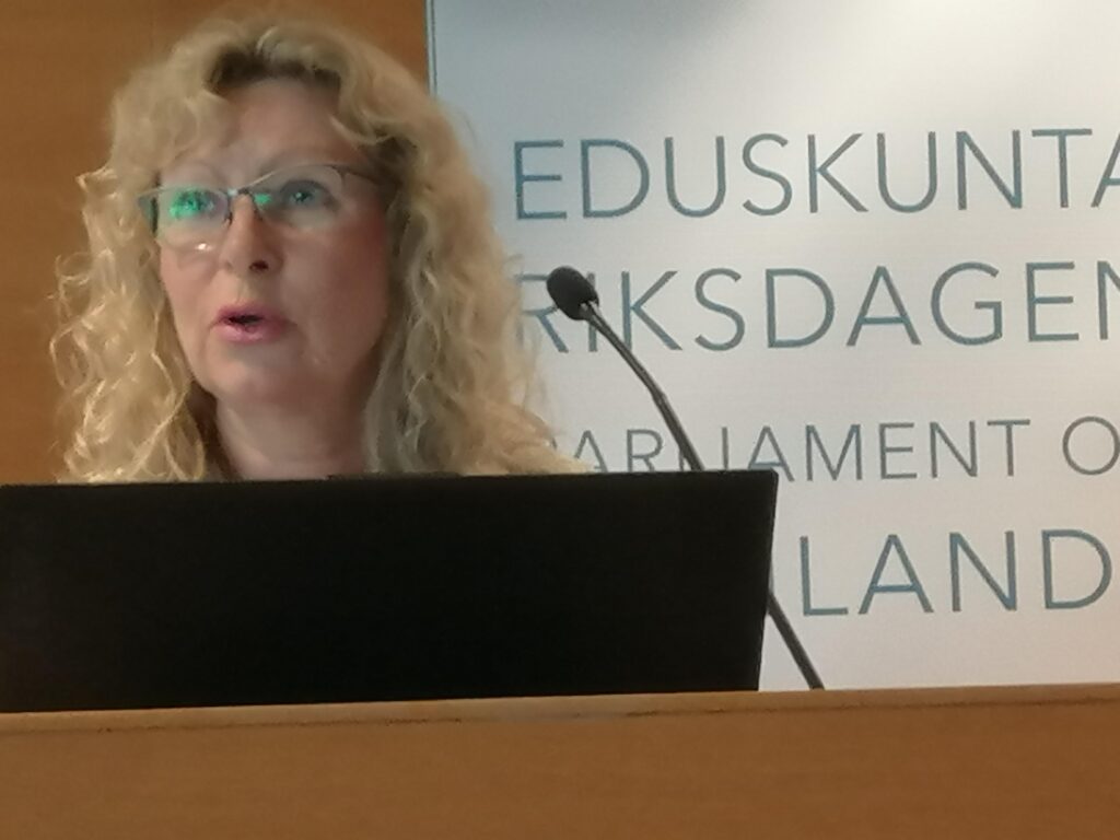 Kokemusasiantuntija Virpi Hyttinen puhujapöntössä taustalla teksti eduskuntanan