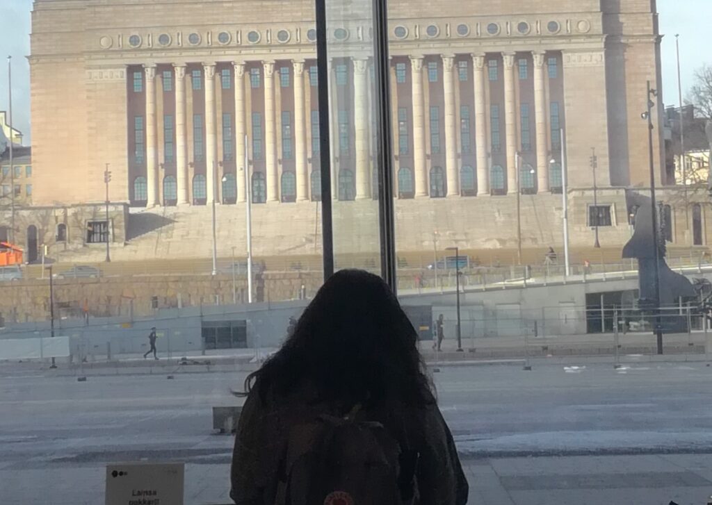 Nainen ikkunan edessä taustalla eduskuntatalo