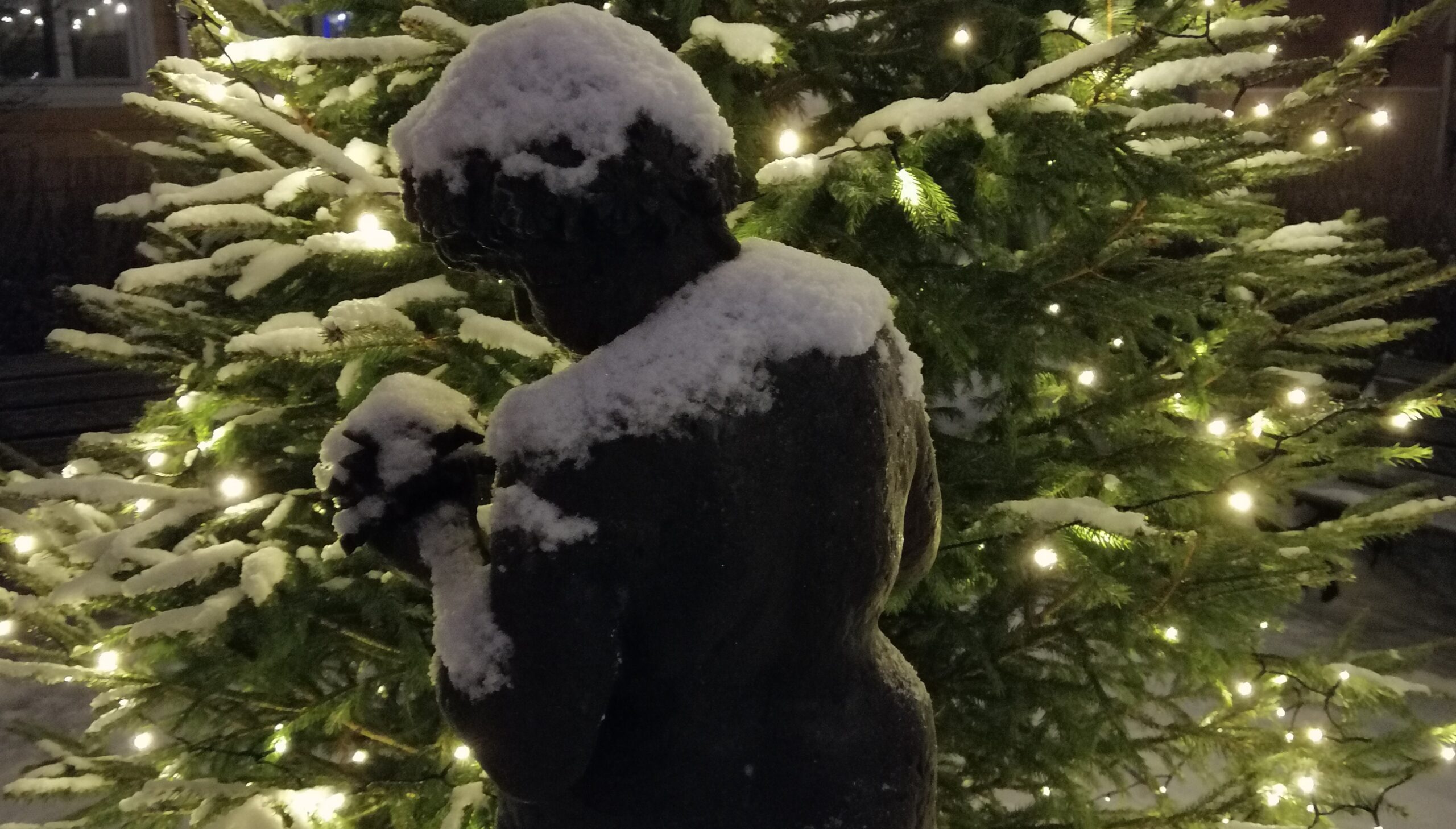 Luminen lapsipatsas valaistun joulukuusen edessä.