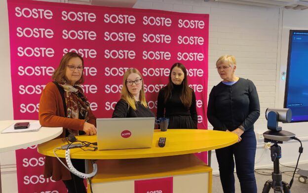 Neljä henkilöä seisomassa esityspöydän ääressä.