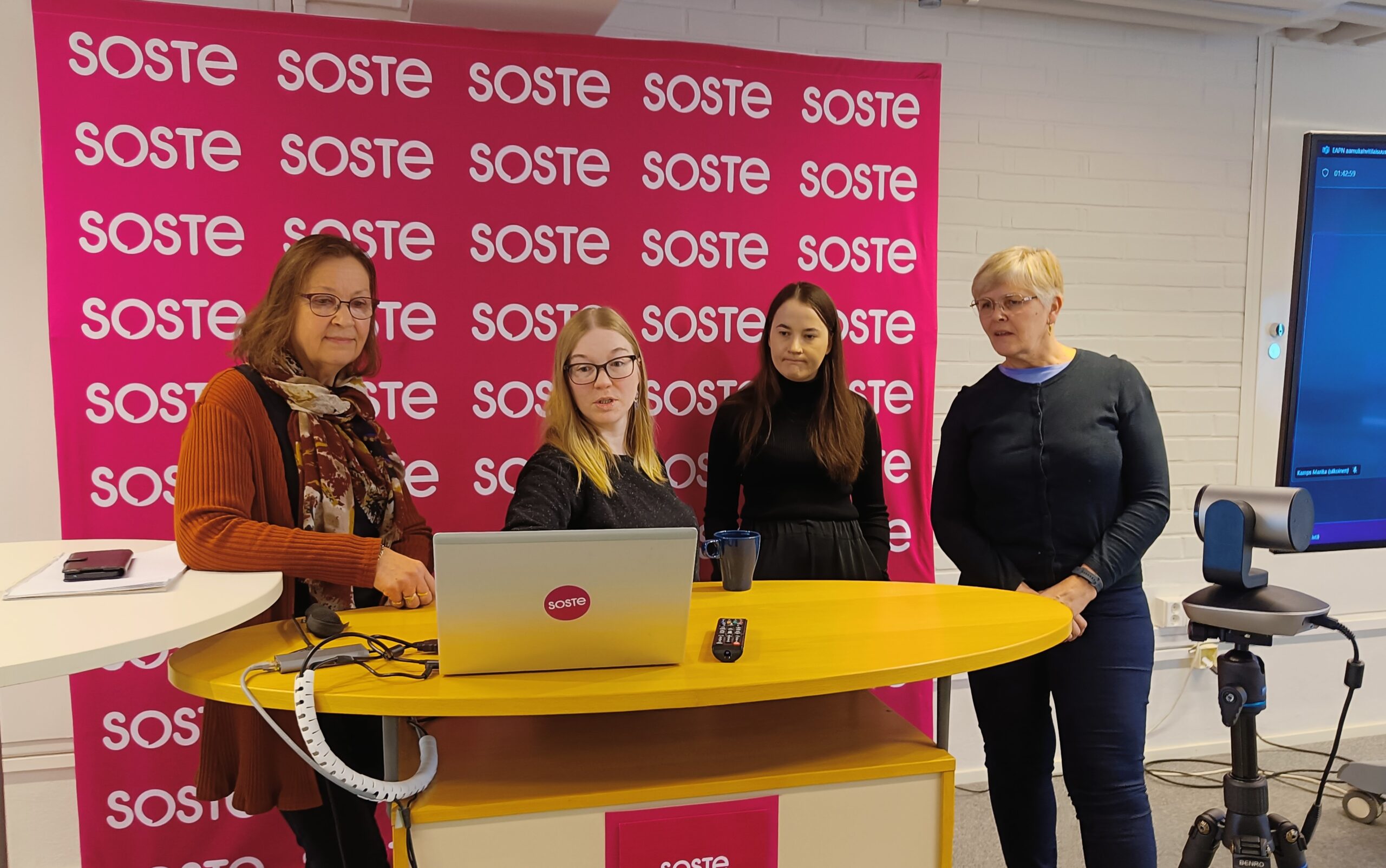 Neljä henkilöä seisomassa esityspöydän ääressä.